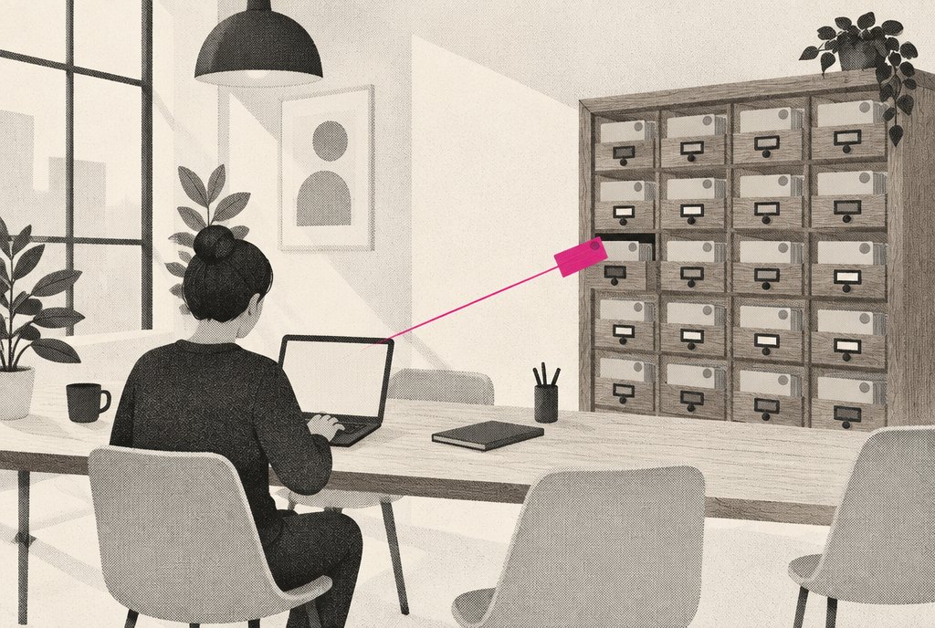 An agency team room where a teammate types on a laptop while a small magenta card slides from the laptop into a wooden card catalogue drawer that already holds many grey cards
